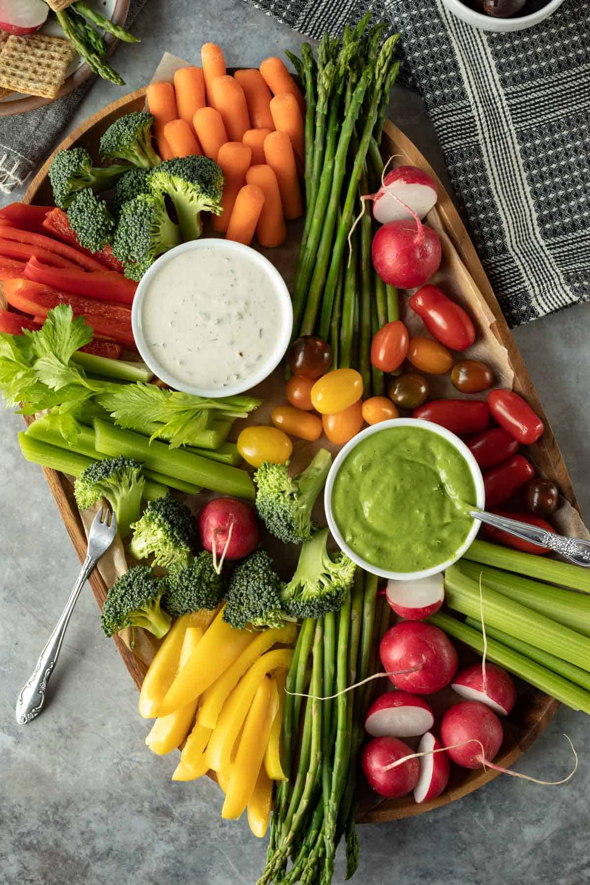 a veggie tray with carrots, yellow pepper, asparagus, radishes, celery, broccoli, and tomatoes.
