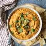 thick and creamy cauliflower buffalo dip in a bowl garnished with cilantro and pumpkin seeds.