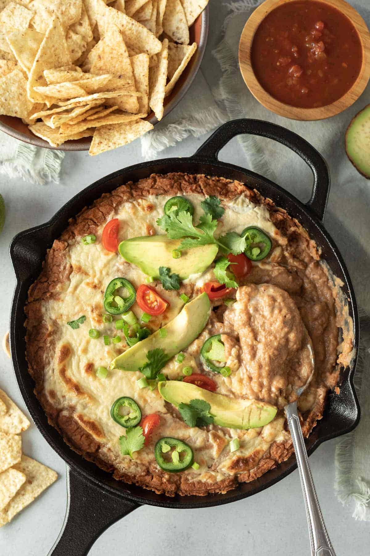 scooping up creamy refried bean dip from a skillet.