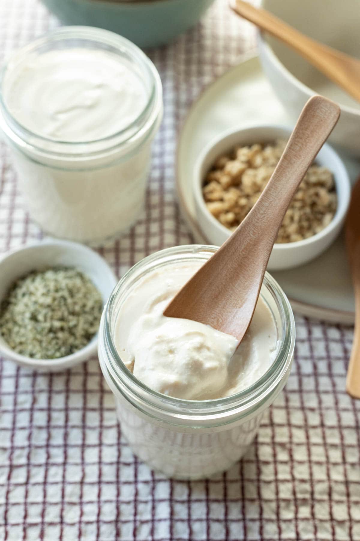 a glass jar of homemade vegan yogurt with toppings nearby.