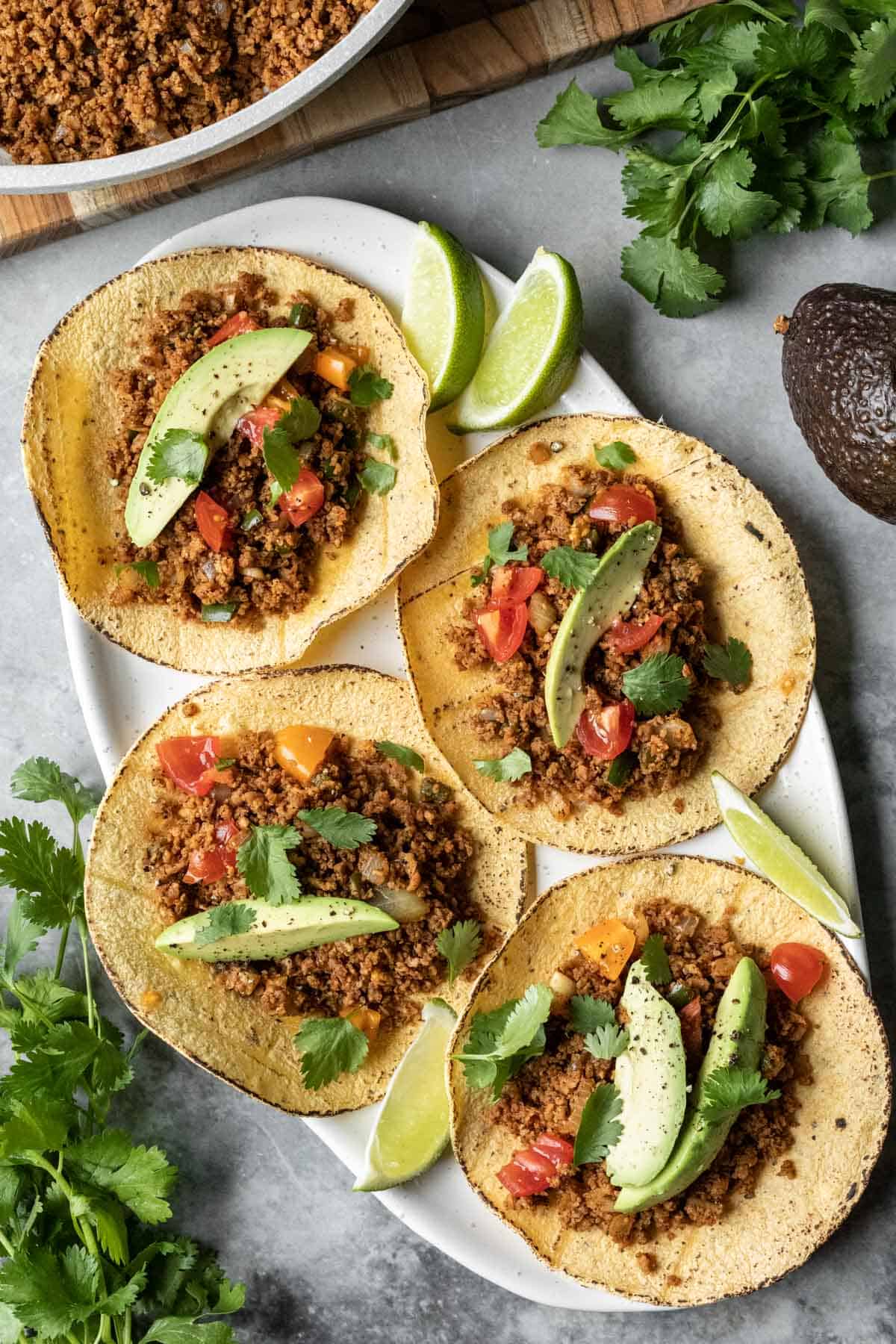 a platter with four vegan tacos made with TVP, corn tortillas, and topped with avocado.