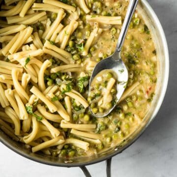a large saute pan filled with white wine pasta sauce, freshly cooked pasta, and peas.