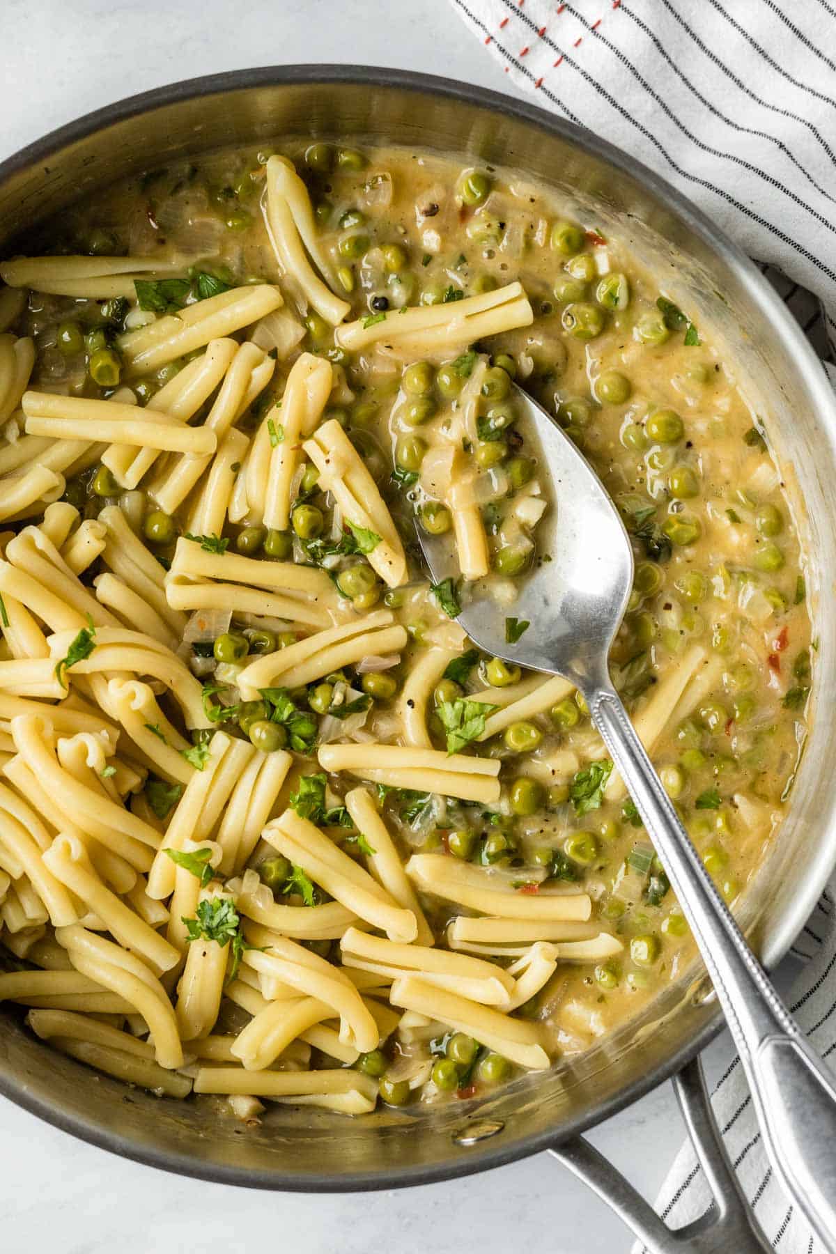 spooning white wine sauce onto pasta in a large saute pan.