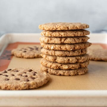 crisp almond flour oatmeal cookies stacked up and resting on a silicone baking mat.