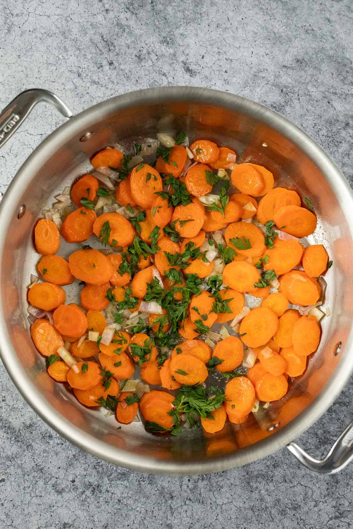 carrot coins and shallot sauteing in oil with finely chopped carrot greens added to the pan.