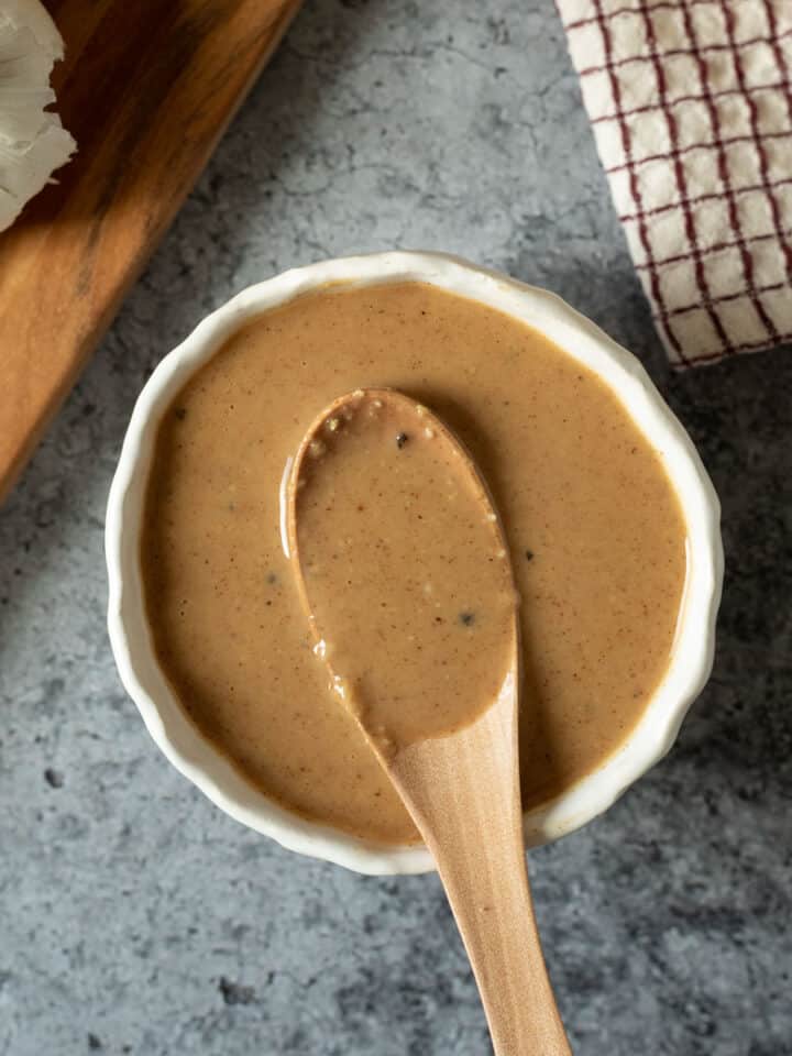 creamy miso sauce and dressing in a small white bowl with ginger and garlic on a cutting board.