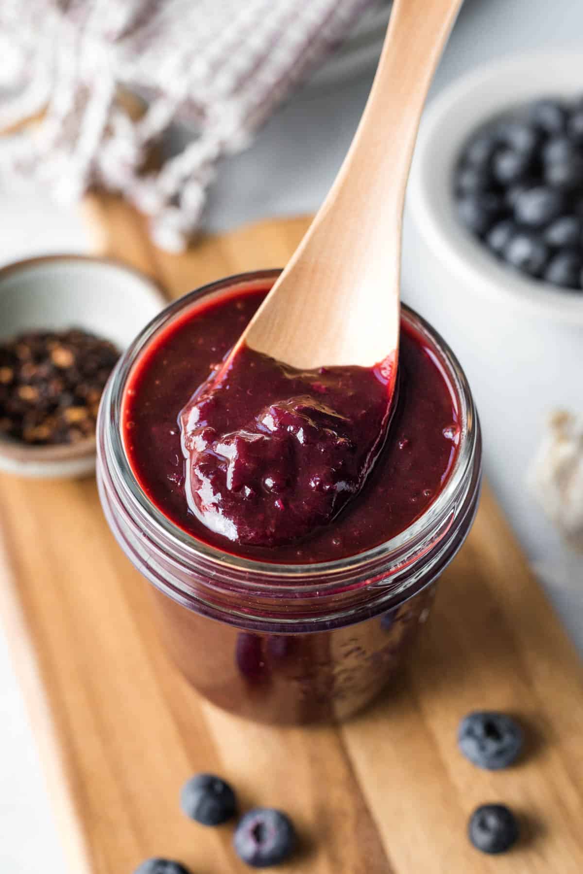 Colorful and thick blueberry barbecue sauce in a glass jar with blueberries in background.