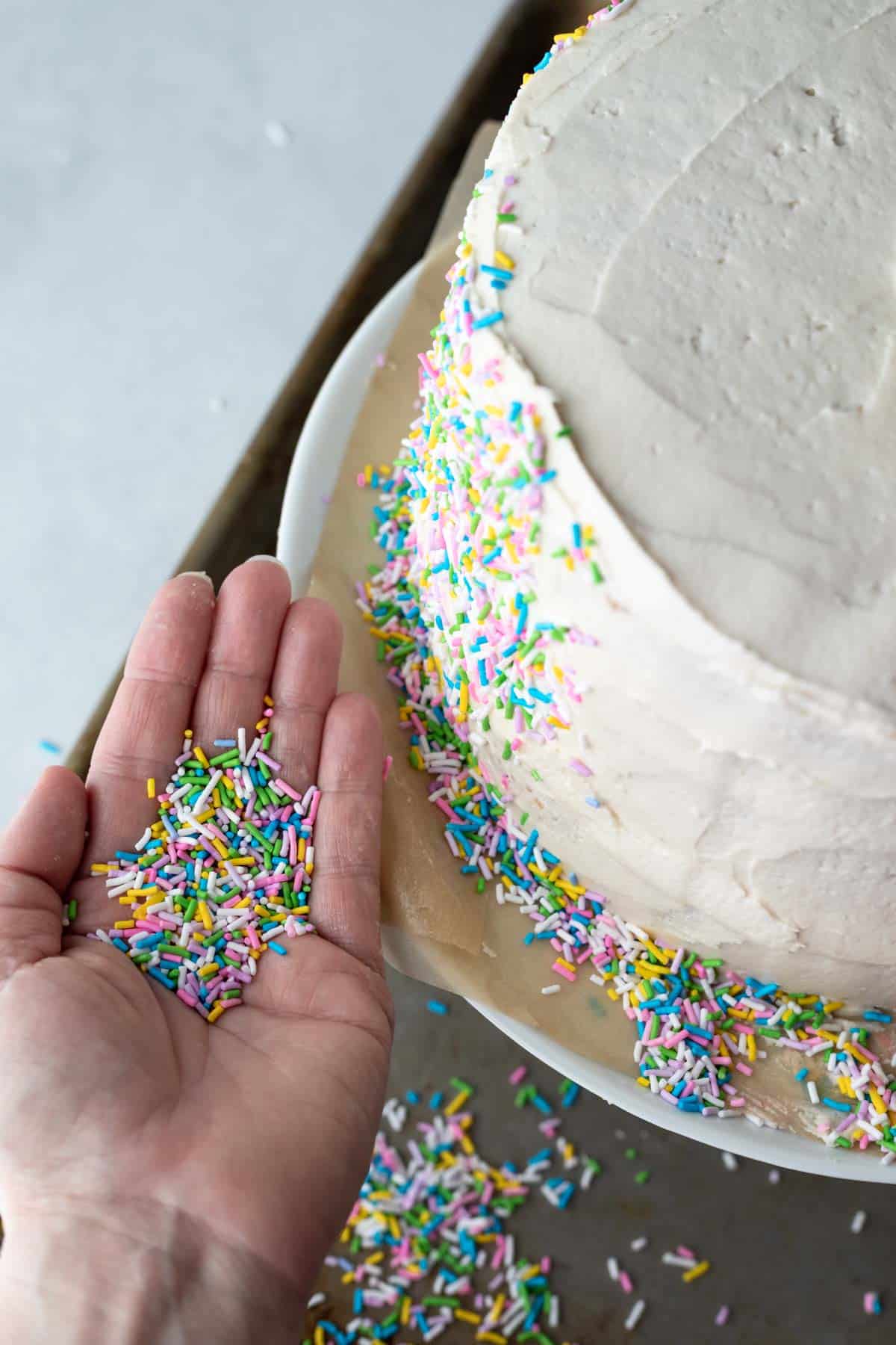 A hand holding a palmful of sprinkles ready to apply to the sides of the cake.
