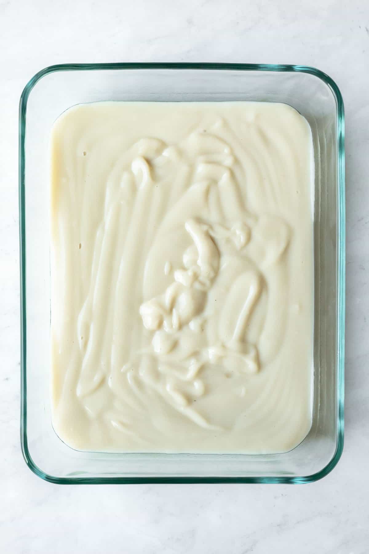Freshly prepared vegan vanilla pudding in a glass container ready to be chilled.