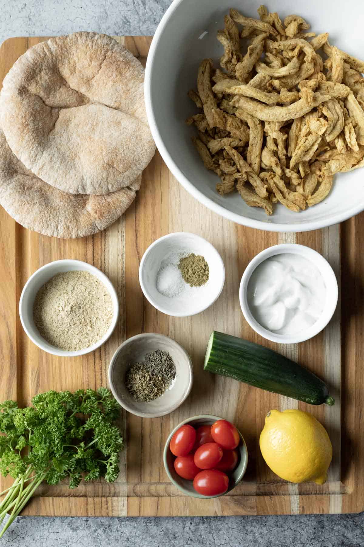 A photo of the ingredients needed for Mediterranean pita sandwiches laid out on a wood cutting board.
