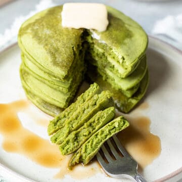 A stack of green spinach pancakes drizzled with maple syrup.