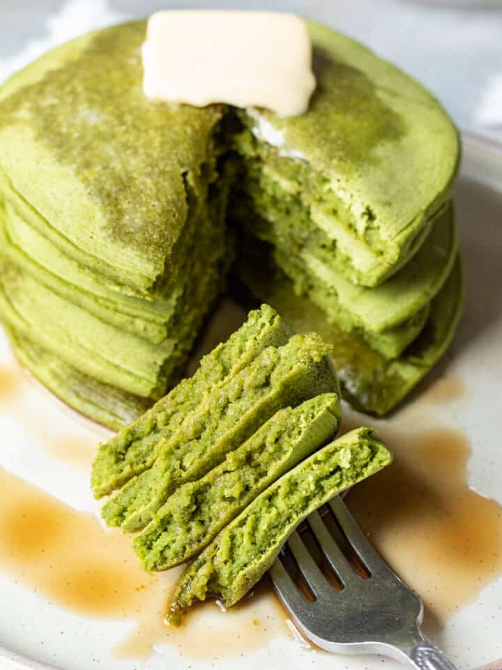 A stack of green spinach pancakes drizzled with maple syrup.