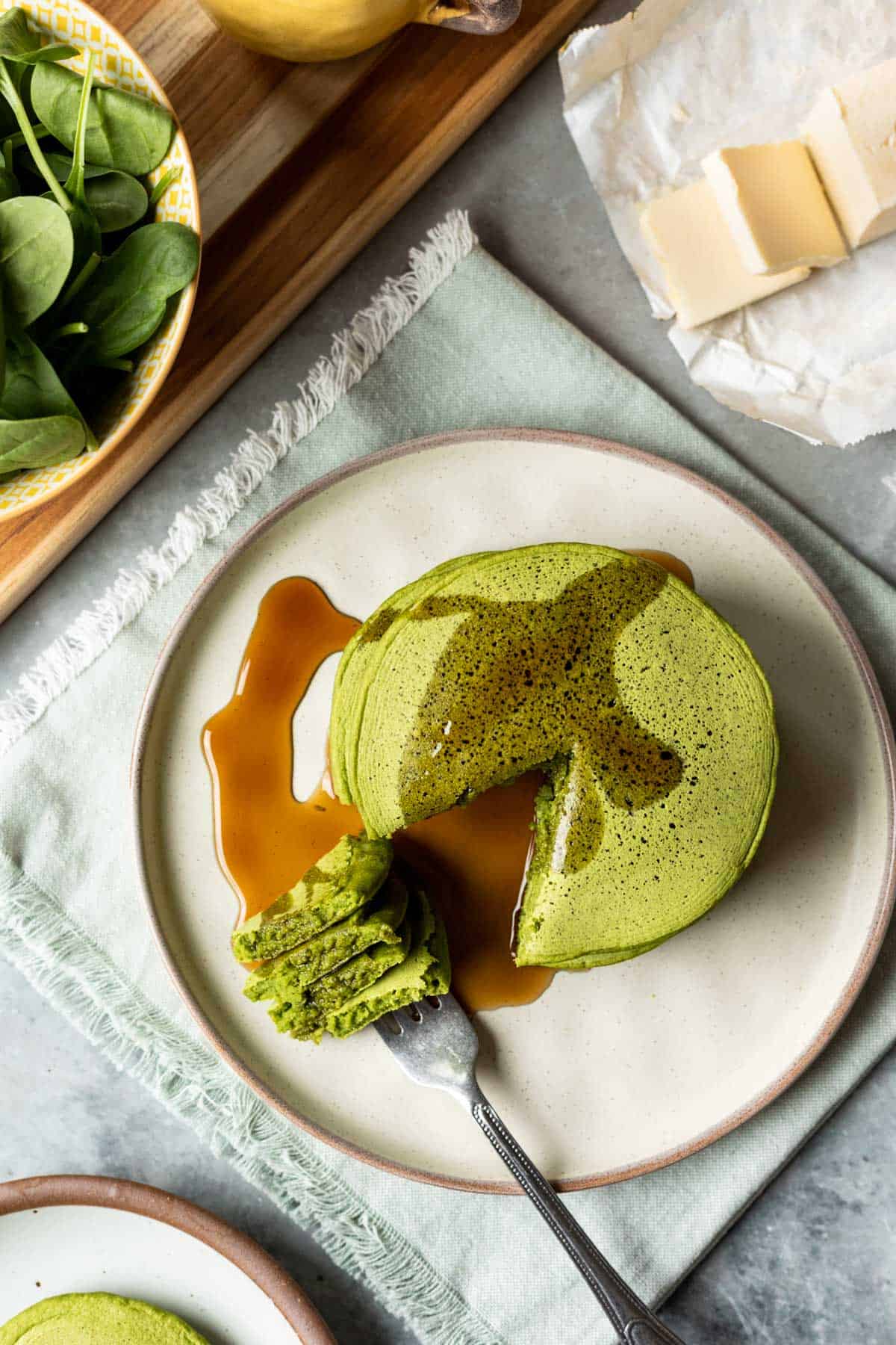 Spinach pancakes on a plate with a bite on a fork and vegan butter nearby.