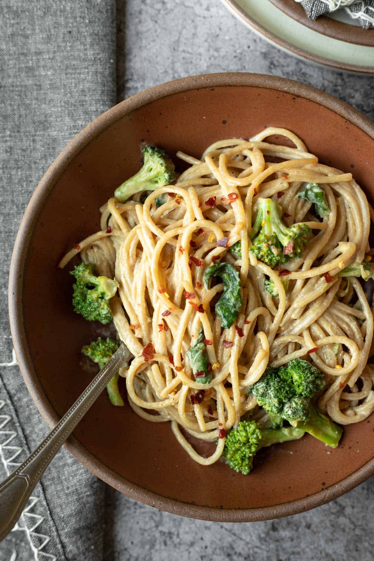 A serving of tahini noodles in a rust-colored pottery bowl on a dark gray background.