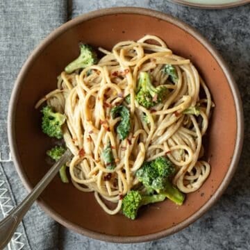 Overhead view of a dark red bowl filled with creamy tahini noodles and broccoli.