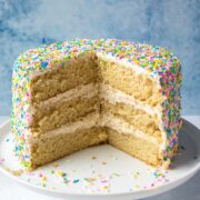A 3 layer vegan vanilla cake decorated with sprinkles with pieces removed to show moist and fluffy texture.