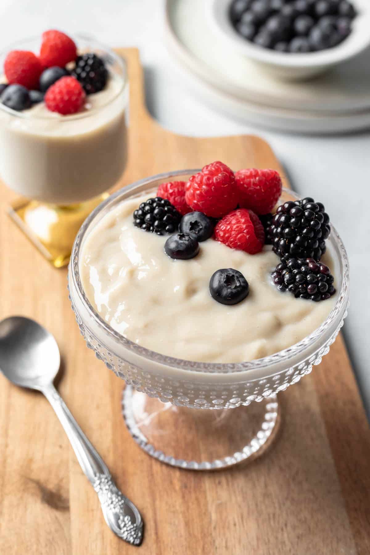 Two fancy glass serving dishes filled with vanilla pudding garnished with fresh berries.