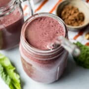 A healthy smoothie made with berries, tofu, greens, and spirulina in a glass jar with a glass straw.