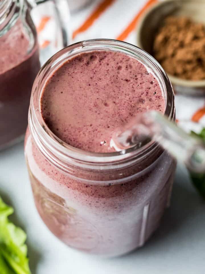 A healthy smoothie made with berries, tofu, greens, and spirulina in a glass jar with a glass straw.