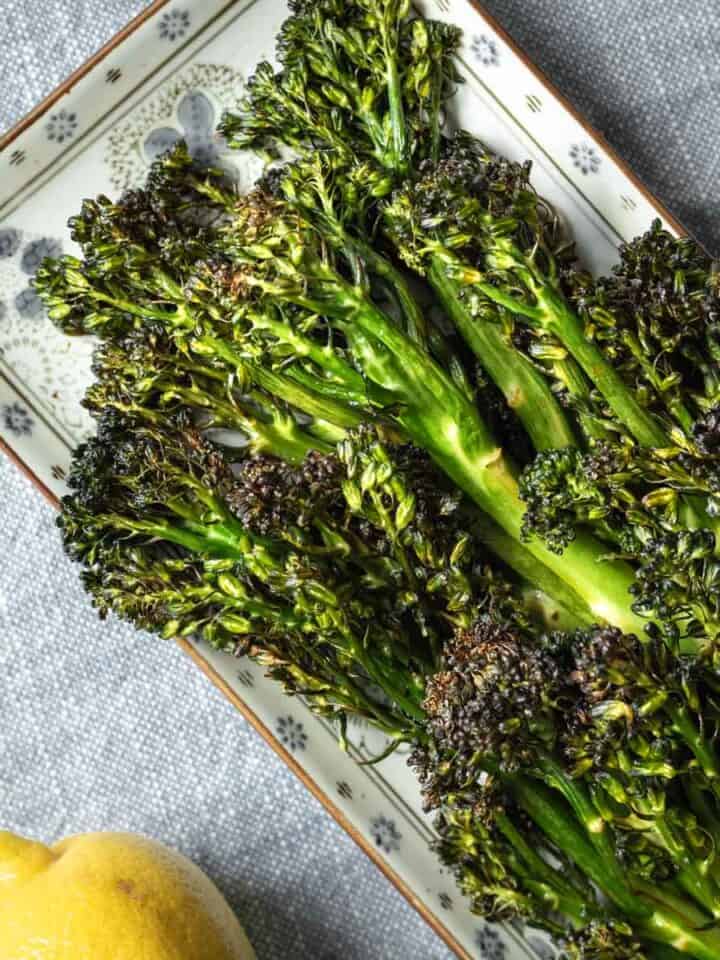 Crispy air fryer broccolini on a small plate with lemon.