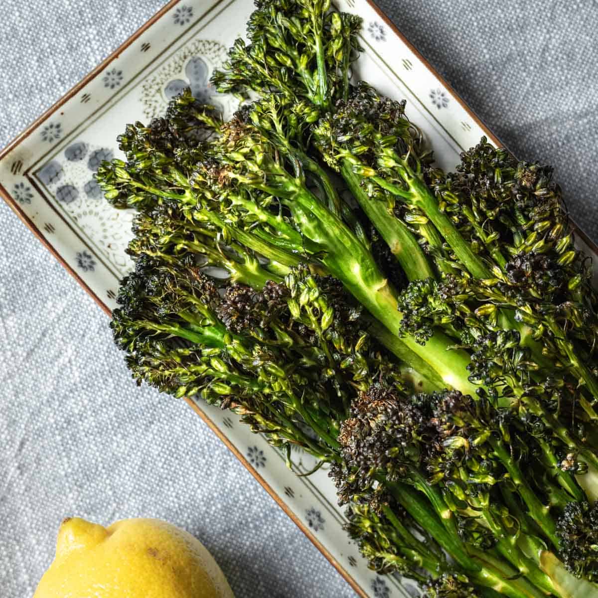 Crispy air fryer broccolini on a small plate with lemon.