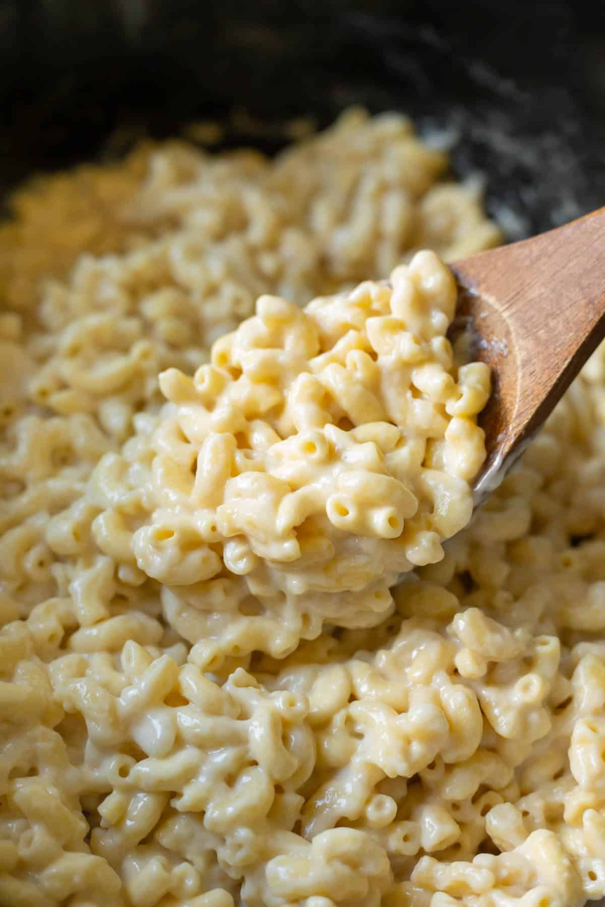 Closeup of creamy vegan mac and cheese inside a Crockpot being scooped up with a wooden spoon.