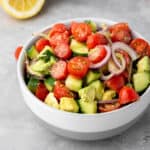 A light gray bowl filled with avocado salad made with tomatoes, cucumber, and red onion.