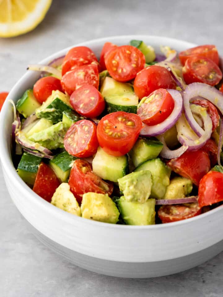A light gray bowl filled with avocado salad made with tomatoes, cucumber, and red onion.