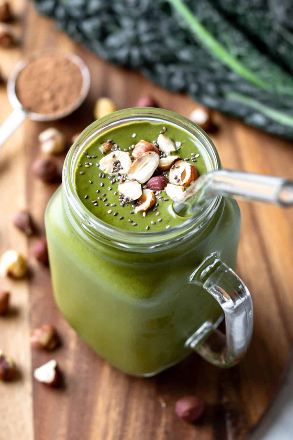 healthy kale smoothie in a glass jar topped with hazelnuts and chia seeds.