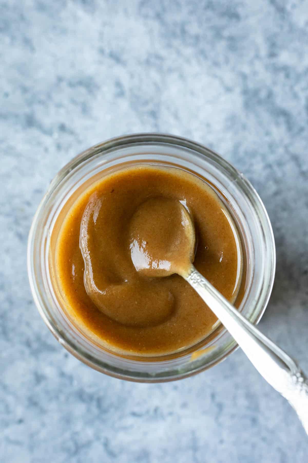 A small spoon scooping date caramel sauce from a jar.
