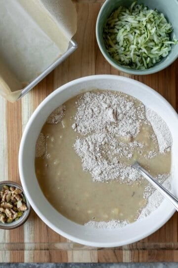Stirring together the batter in a bowl with grated zucchini in a separate bowl.