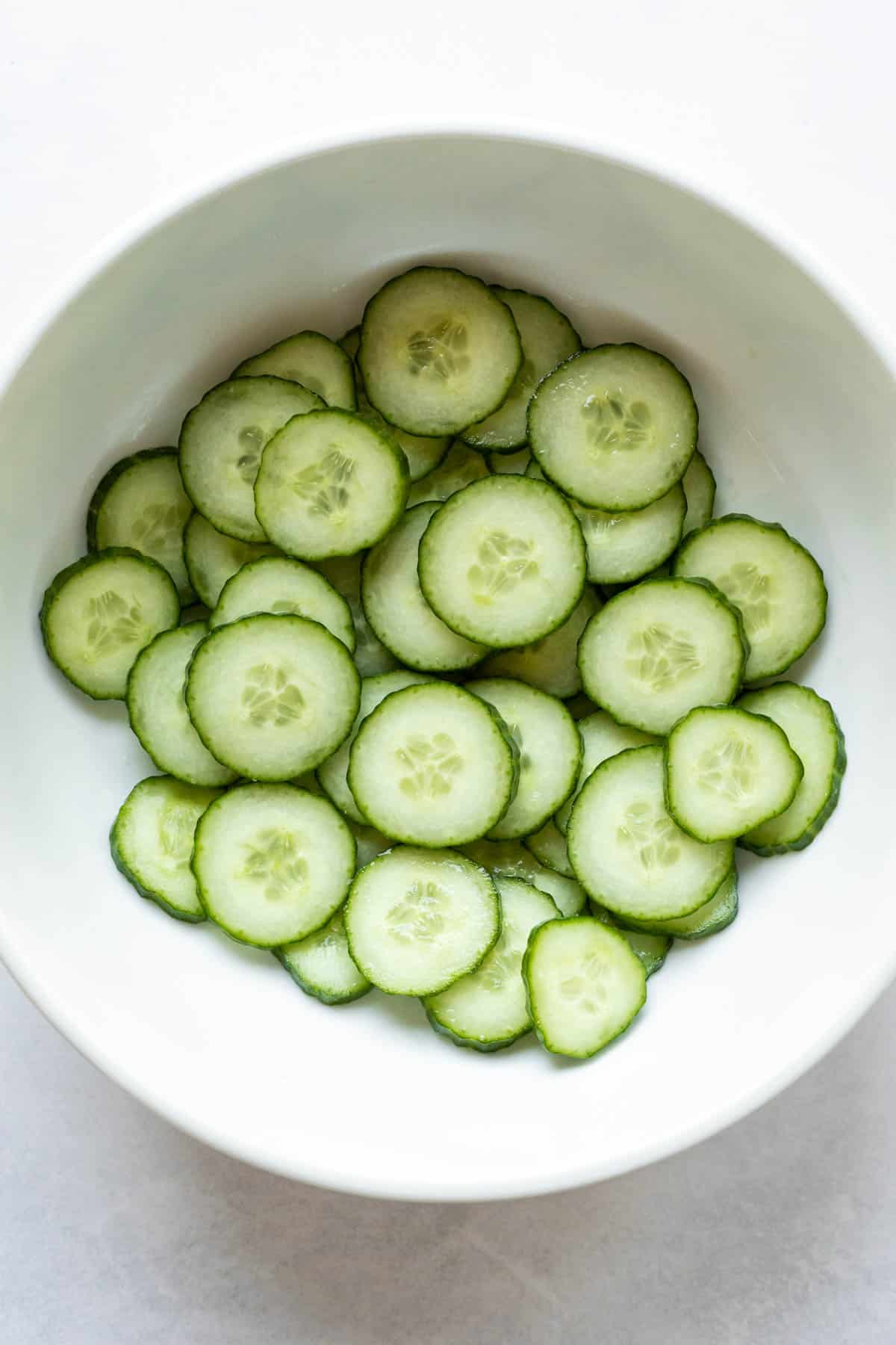 Large bowl filled with sliced English cucumber that has been salted to draw out moisture.