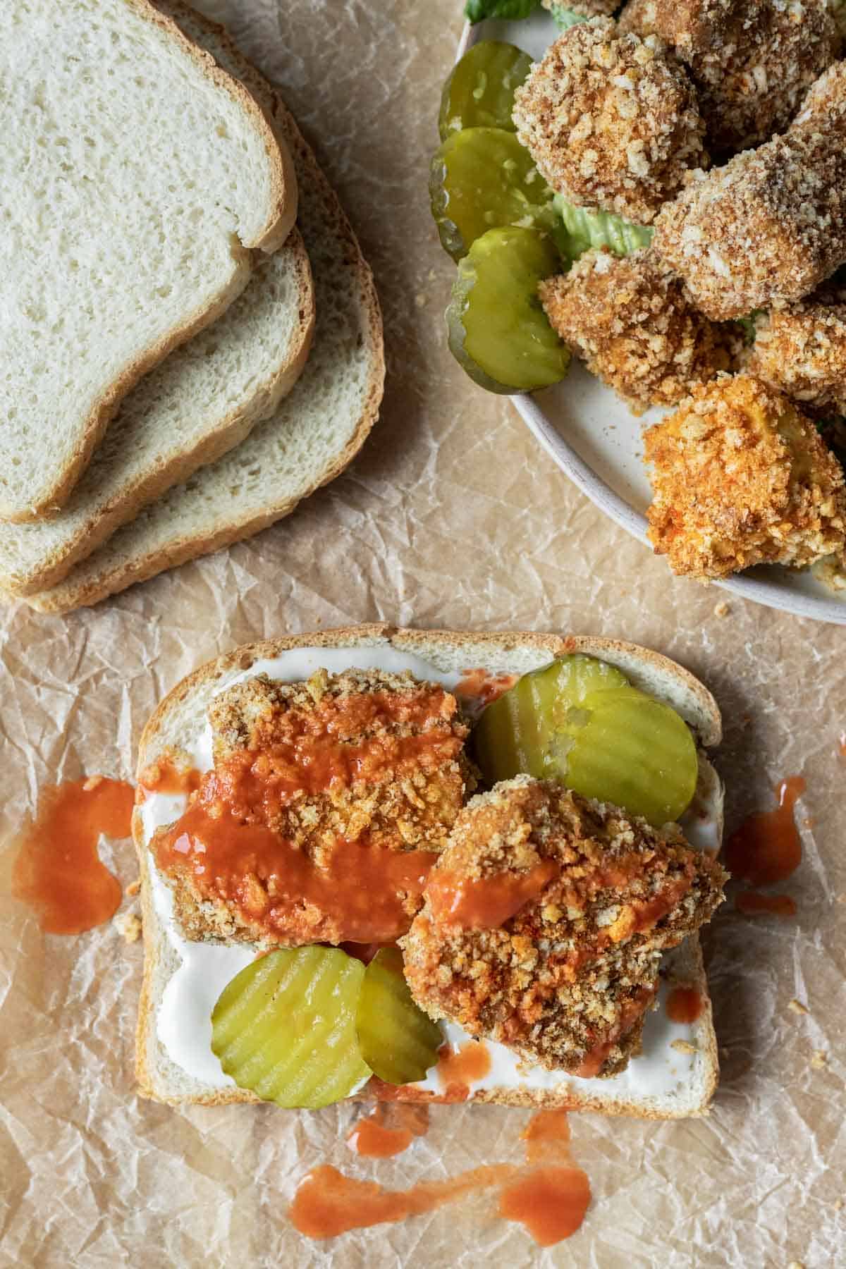 Two pieces of crispy breaded hot tofu on white bread with pickle slices.