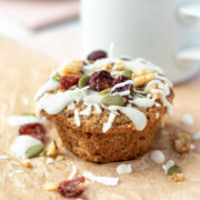 close up of a muffin topped with glaze, seeds, nuts, and dried fruit