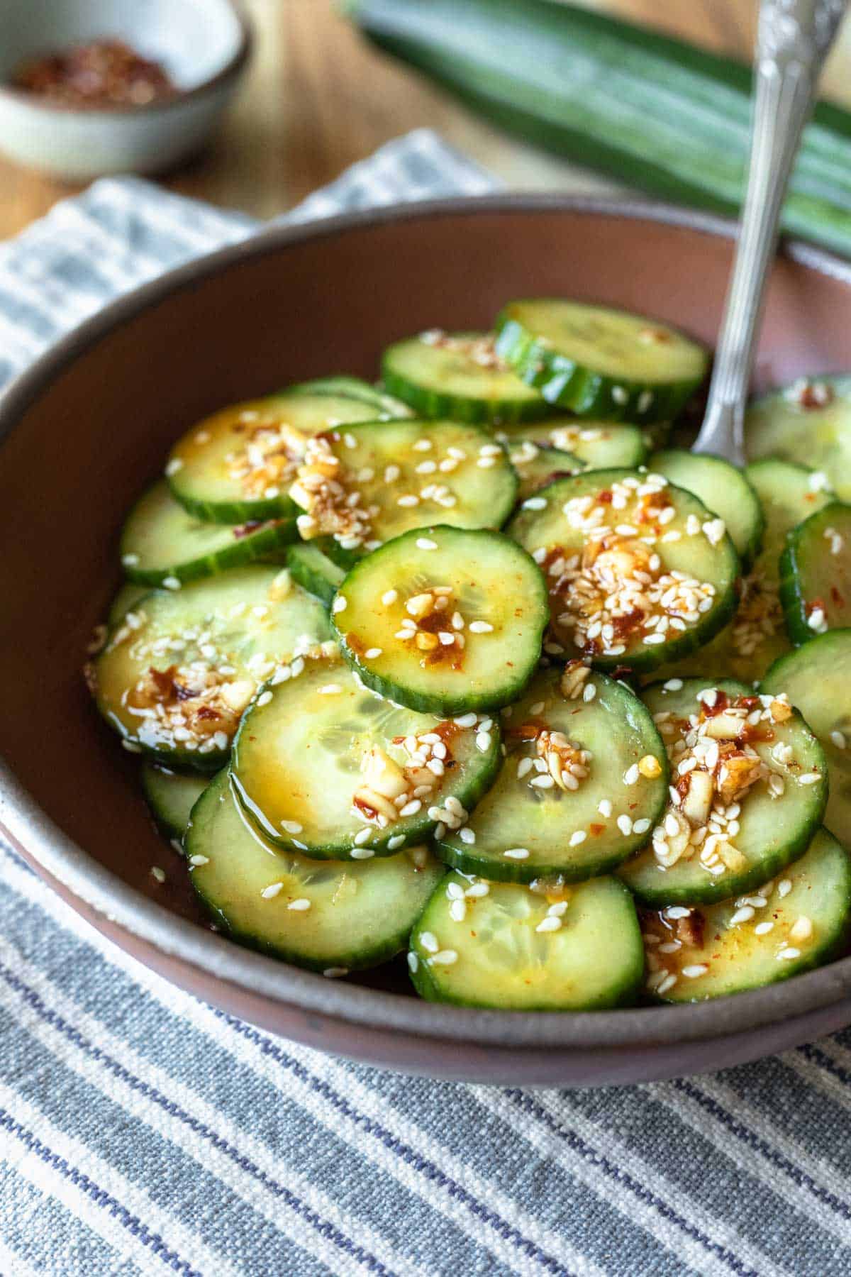 Serving bowl filled with spicy cucumber salad garnished with sesame seeds and chile flakes.