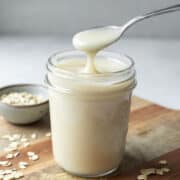 A small spoon filled with condensed oat milk resting on top of a jar to show the thick consistency.