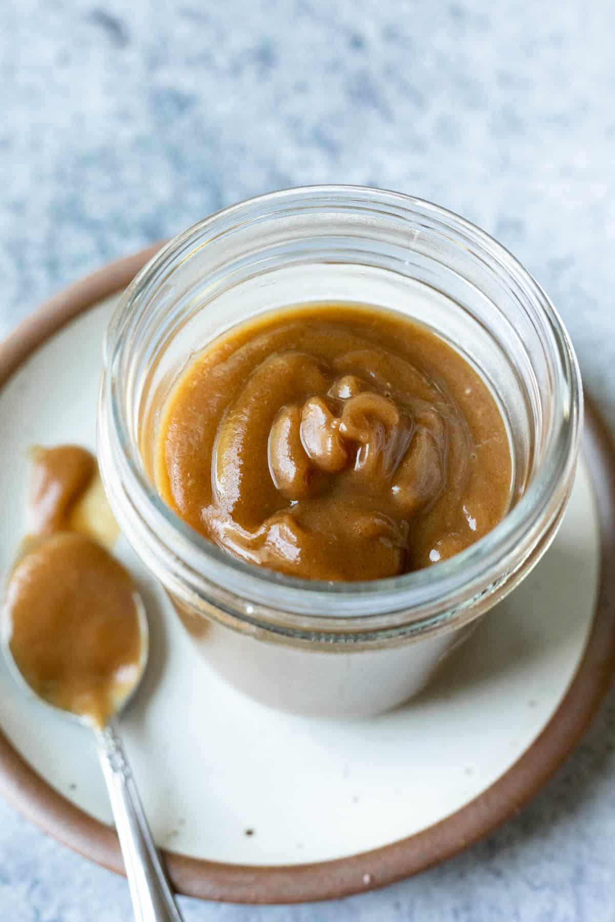 A spoon with date caramel sauce on it resting beside a full jar.