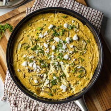 Baked vegan frittata in a pan topped with feta, green onion, and parsley.