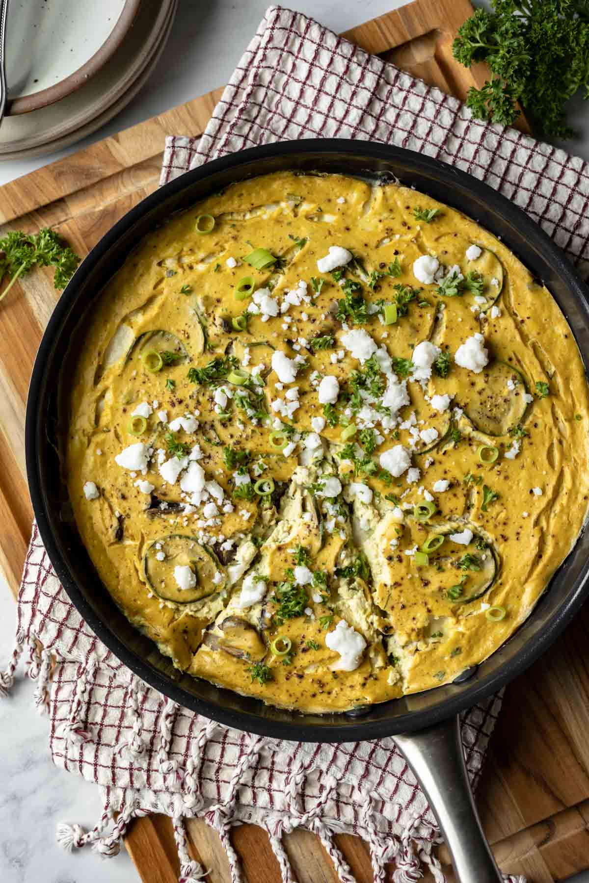 Vegan tofu frittata in a non-stick skillet topped with dairy-free feta and herbs.