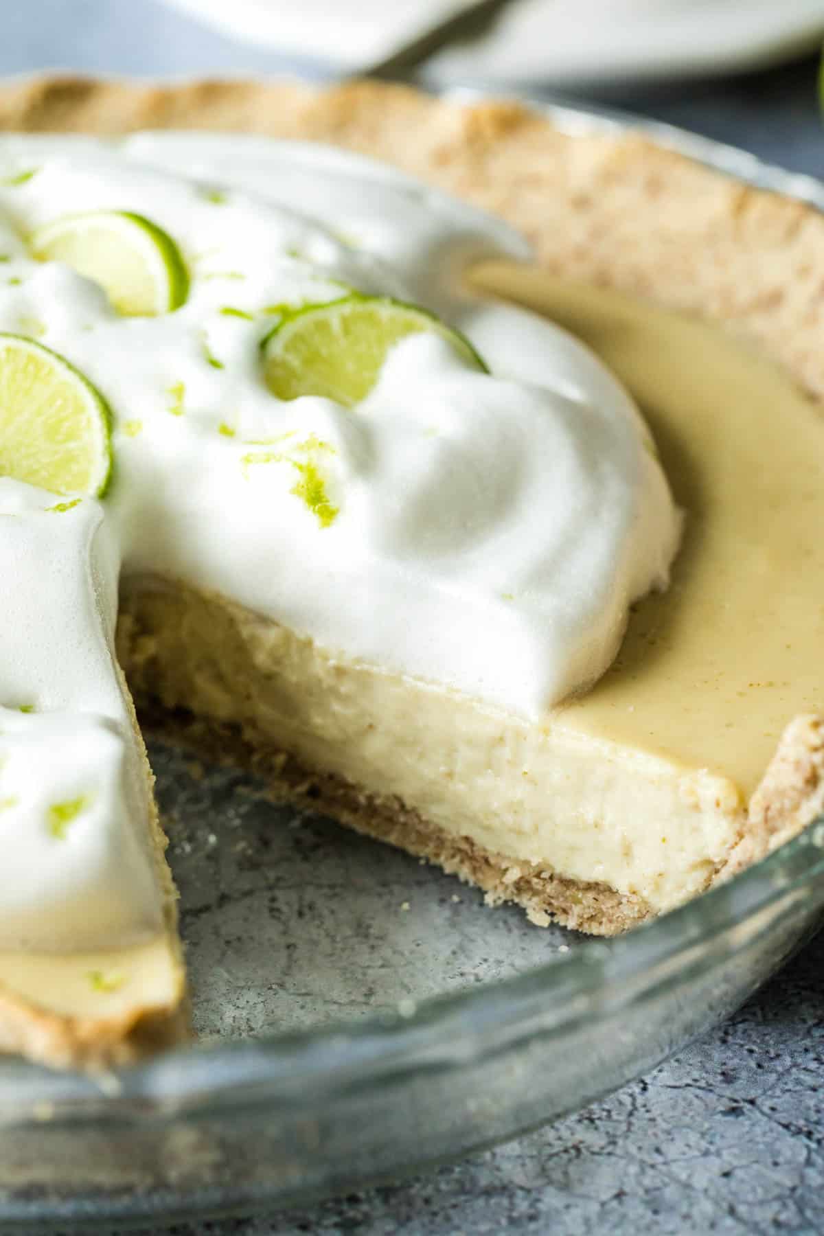 Key lime pie in a glass pie plate with a slice removed so you can see the inside of the creamy tofu filling.