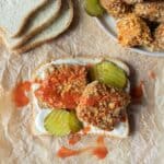 A piece of bread topped with vegan mayo, pickles, and two pieces of Nashville hot tofu drizzled with hot sauce.