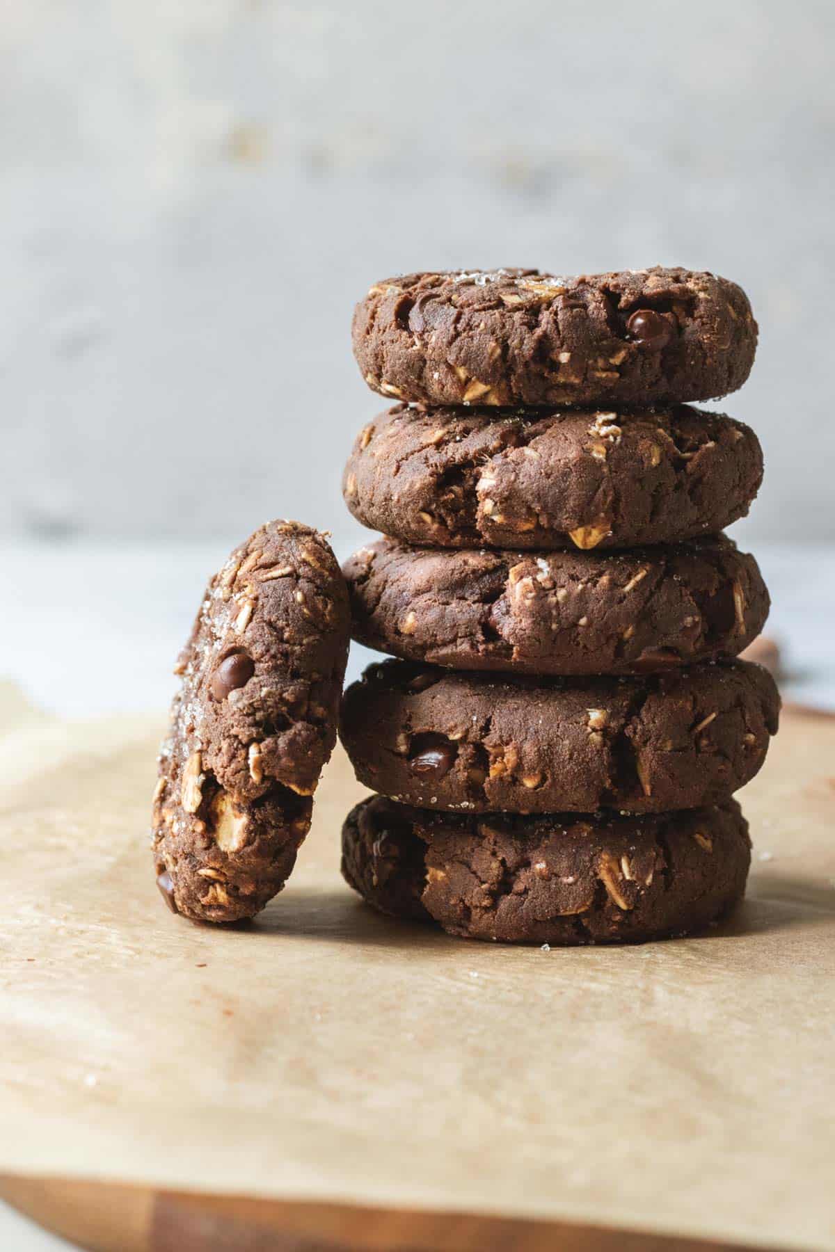 Vegan chocolate protein cookies stacked on parchment paper against a gray background.