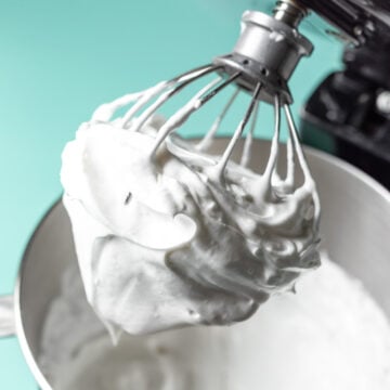 Thick vegan whipped cream clinging to the whisk of a stand mixer.