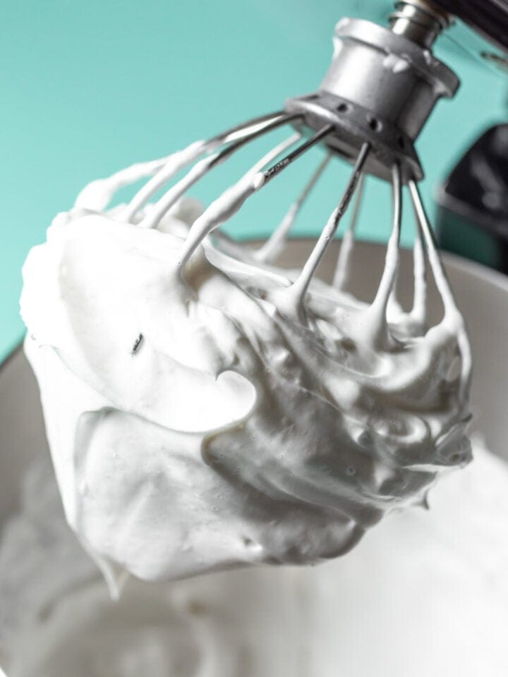 Thick vegan whipped cream clinging to the whisk of a stand mixer.