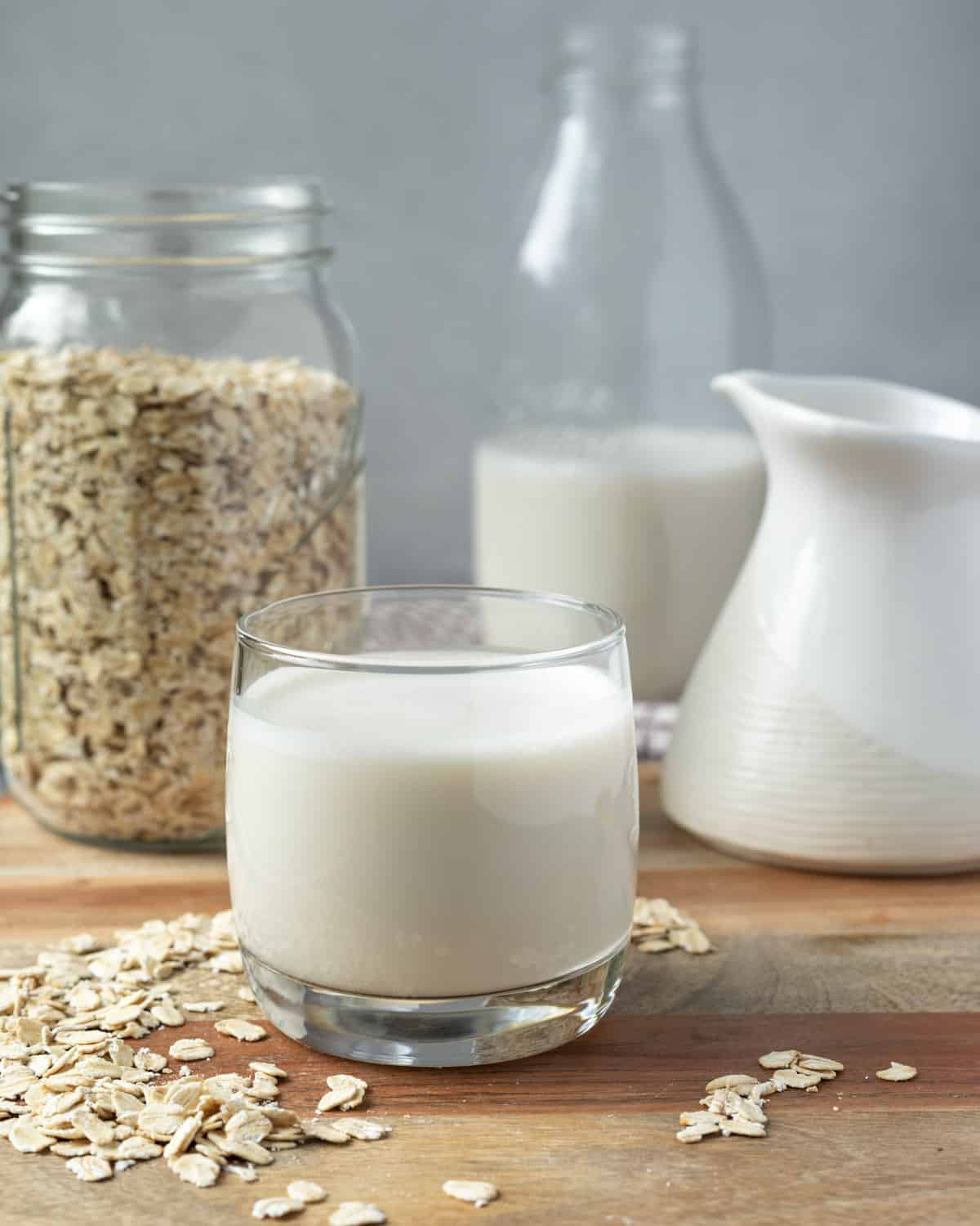 A glass of homemade oat milk on a wood board with a glass jar of milk in the background.
