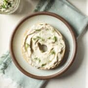 Half of a bagel spread with tofu cream cheese and sprinkled with dill resting on a small plate.