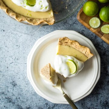 A slice of vegan key lime pie topped with aquafaba whipped cream with the rest of the pie nearby.