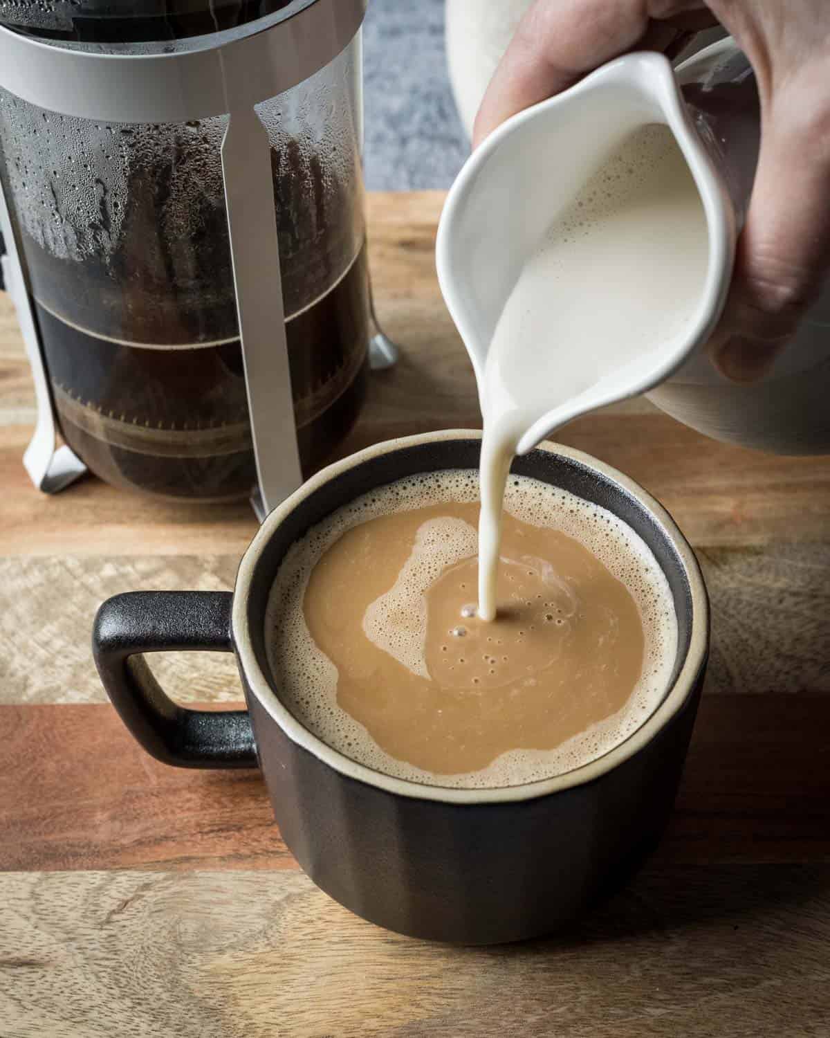 Pouring homemade oat milk into a cup of coffee.