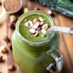A thick green kale smoothie in a glass mug topped with chia seeds and hazelnuts.