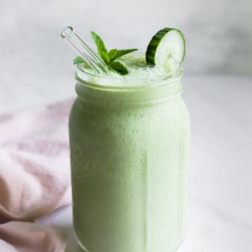 A light green, creamy cucumber smoothie in a glass Ball jar with a glass straw.